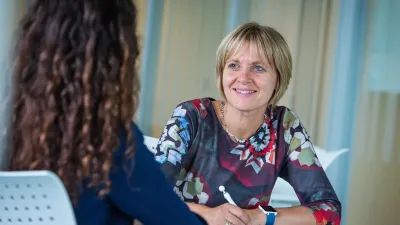 Vrouw die glimlacht en aan een tafel zit met een andere vrouw