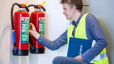 Man met geel veiligheidshesje controleert de brandblusser